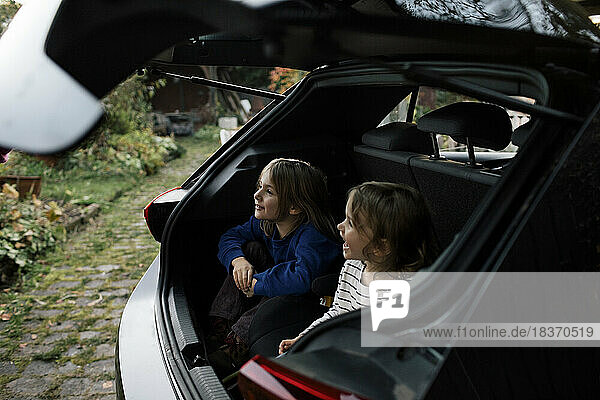Glückliche Schwestern  die sich im Kofferraum eines Elektroautos vergnügen