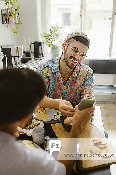 Mann teilt Smartphone mit Freund beim Essen zu Hause