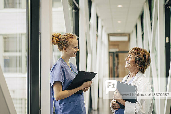 Side view of female healthcare workers discussing while standing in corridor