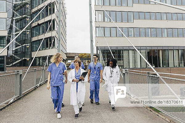 Multirassisches Gesundheitspersonal diskutiert beim Spaziergang auf der Brücke neben dem Krankenhausgebäude