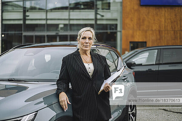 Porträt einer selbstbewussten Verkäuferin mit Dokumenten neben einem Auto stehend