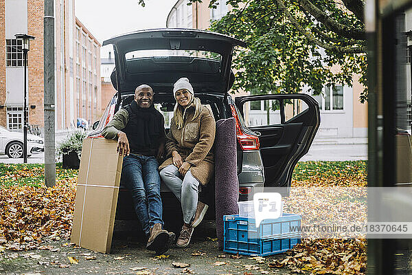 Porträt eines lächelnden reifen Paares mit Pappkarton und Kiste im Auto sitzend im Herbst