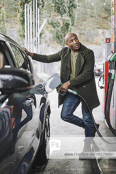 Reifer Mann schaut weg  während er sein Auto an einer Tankstelle auftankt