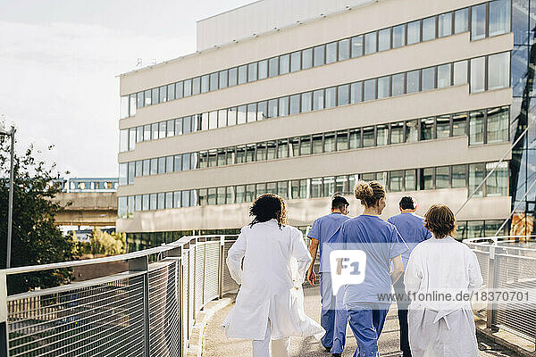 Männliches und weibliches Gesundheitspersonal auf einer Brücke  die zum Krankenhaus führt