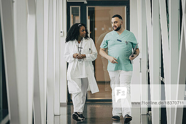 Male and female healthcare workers talking while walking in corridor at hospital