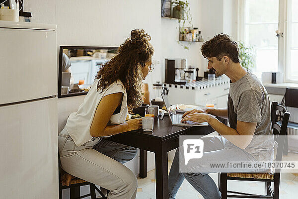 Man talking to woman while using laptop on dining table at home