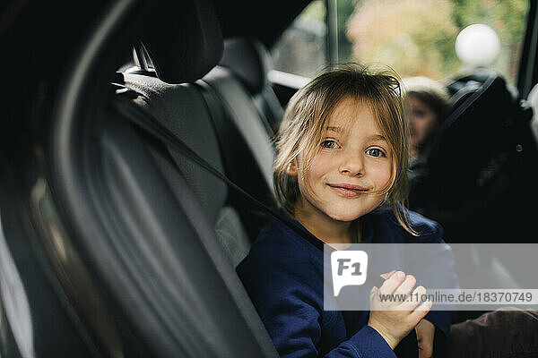 Porträt eines lächelnden Mädchens  das den Sicherheitsgurt hält  während es im Auto sitzt