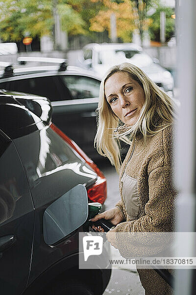 Reife Frau mit blondem Haar beim Tanken im Auto an der Tankstelle