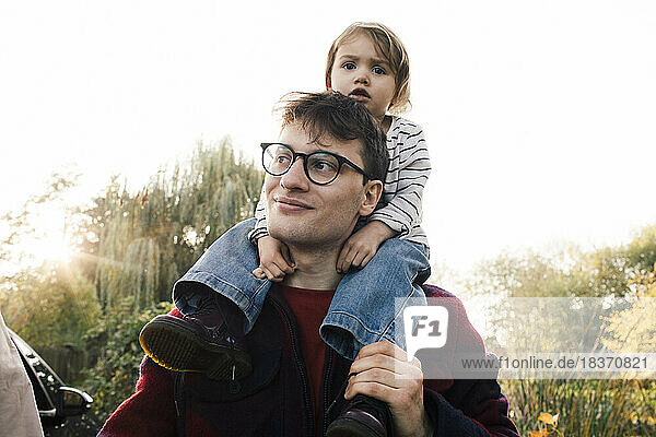 Lächelnder Vater mit Brille  der seine Tochter auf der Schulter trägt