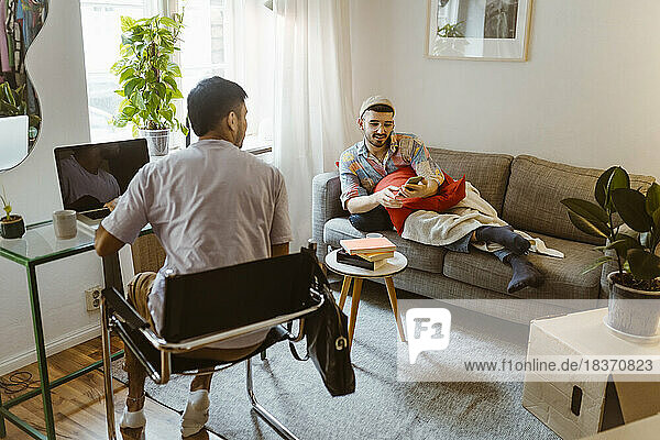 Man sitting on chair talking to boyfriend using smart phone in living room at home