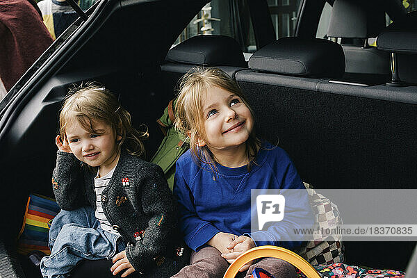 Lächelnde Mädchen sitzen zusammen im Kofferraum eines Elektroautos