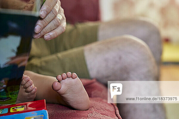 Close up of grandfather reading to toddler  view of the child's bare feet and grandpa's knees.