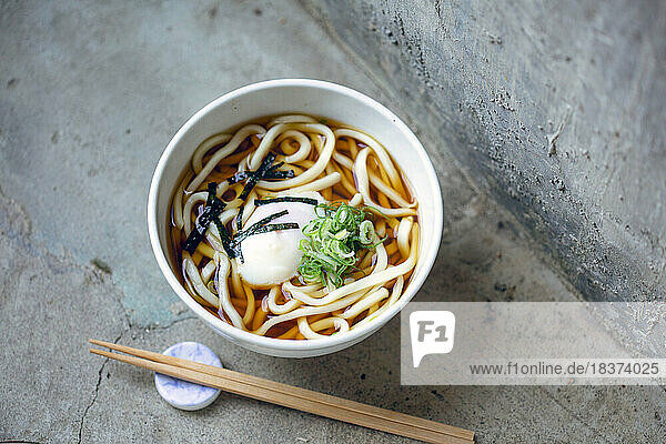 A bowl of noodles  vegetables and broth and a set of chopsticks.