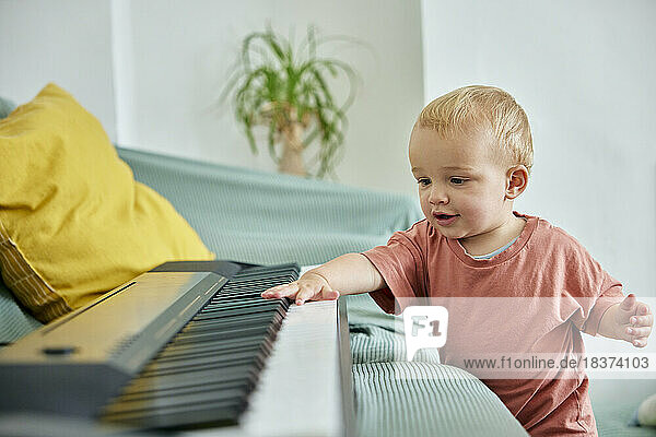 Toddler playing with electronic piano keyboard on sofa