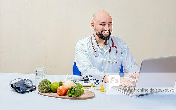 Ernährungswissenschaftler Arzt mit Laptop am Arbeitsplatz. Bärtiger Ernährungswissenschaftler Arzt arbeitet am Laptop am Schreibtisch  Lächelnder Ernährungswissenschaftler mit Laptop am Schreibtisch