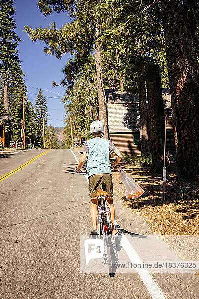 USA  California  Tahoe City  Rear view of boy (12-13) riding bicycle on road