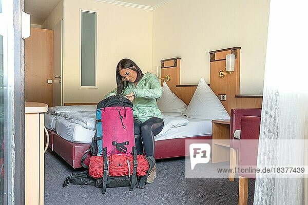 Attractive hiking woman sitting on a hotel bed and looking into her big backpack  Bad Wildbad  Black Forest  Germany  Europe