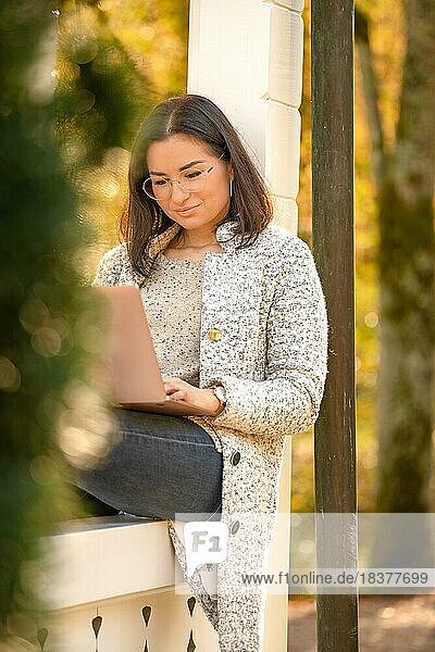 Hübsche Frau mit Brille und MacBook in der Hand sitzt im Park zur Herbstzeit  Bad Liebenzell  Schwarzwald  Deutschland  Europa