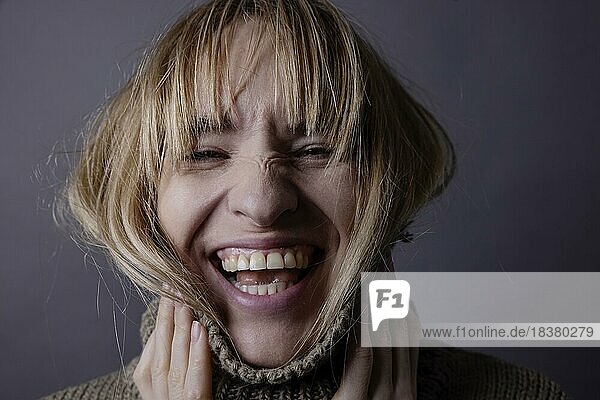 Junge Frau mit Rollkragenpullover und langem Haar lacht in Kamera  Portrait  Studioaufnahme