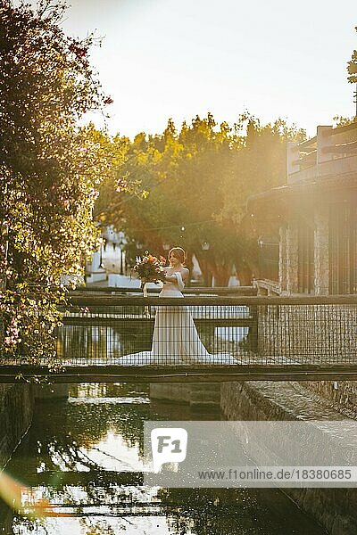 Schöne Braut steht auf hölzernen rustikalen Brücke über einen Fluss bei Sonnenuntergang Zeit