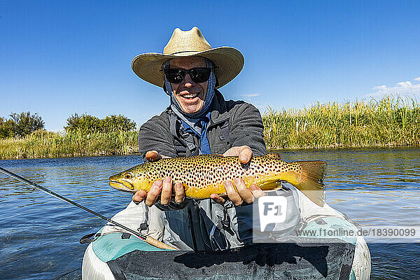 Senior fly fisherman holds brown trout before releasing back into spring creek