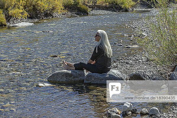 senior blonde woman sits along creek