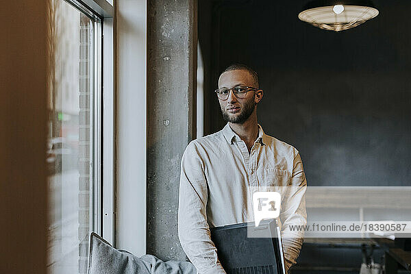Portrait of young businessman with laptop standing in startup company