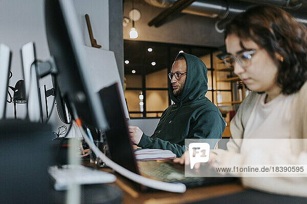 Junger männlicher Computerprogrammierer arbeitet mit einer weiblichen Kollegin am Schreibtisch in einem kreativen Büro