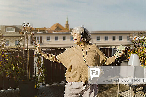 Sorglose ältere Frau  die auf der Terrasse stehend Musik über Kopfhörer hört