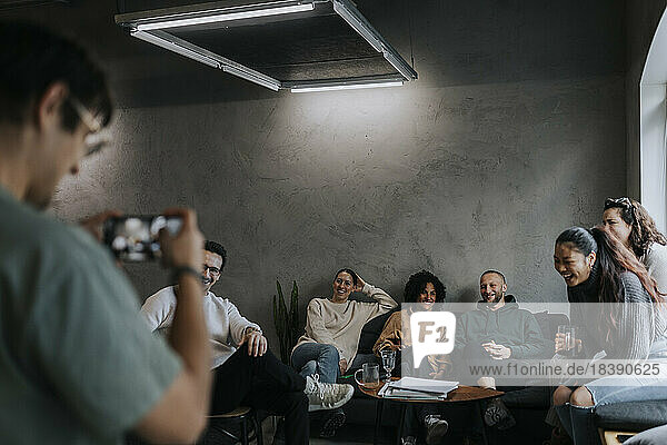 Männlicher Unternehmer fotografiert glückliche Kollegen mit dem Handy in einem Start-up-Unternehmen