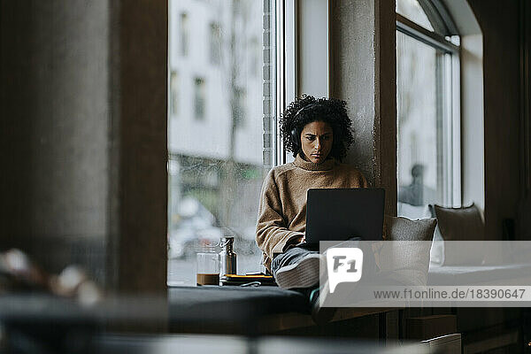 Geschäftsfrau arbeitet am Laptop am Fenster in einem kreativen Büro