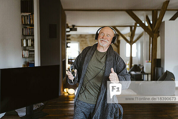 Senior man gesturing while enjoying listening to music through headphones at home