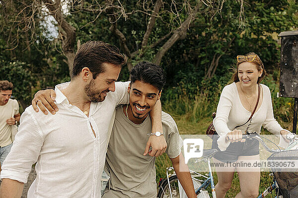 Happy woman with bicycle looking at male friends walking together