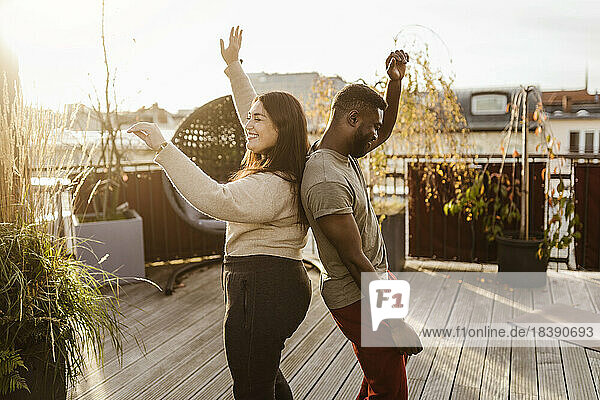 Seitenansicht eines unbekümmerten Paares  das Rücken an Rücken auf einer Terrasse tanzt