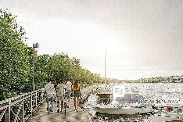 Rückansicht von männlichen und weiblichen Freunden  die gemeinsam auf dem Pier in der Nähe des Jachthafens spazieren gehen