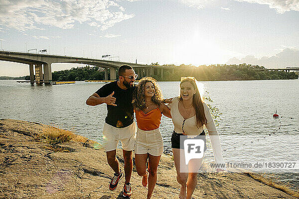 Glücklicher Mann zeigt das Shaka-Zeichen  während er mit seinen Freundinnen beim Picknick auf einem Felsen am Meer spazieren geht