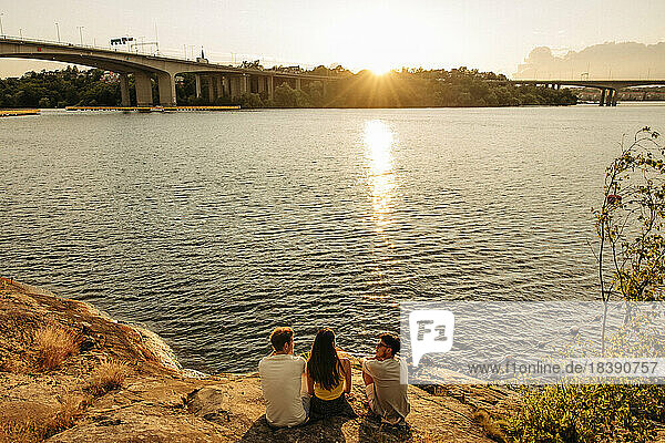 Hohe Winkel Ansicht von Freunden sitzen und reden auf Felsen in der Nähe von Meer bei Sonnenuntergang