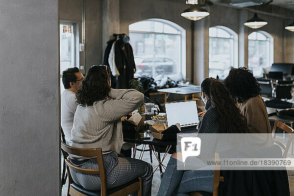 Junger Programmierer bei der Arbeit am Laptop mit männlichen und weiblichen Kollegen beim Mittagessen in einem Start-up-Unternehmen