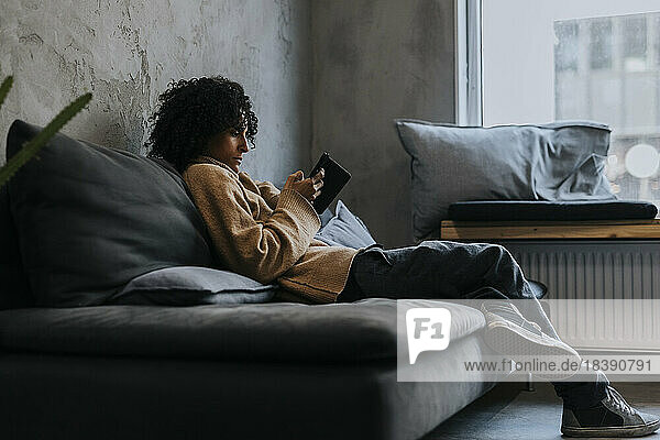 Geschäftsfrau schreibt Textnachrichten über ihr Mobiltelefon  während sie auf dem Sofa eines Start-up-Unternehmens sitzt