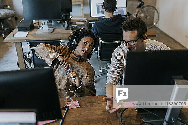 Lächelnder männlicher Hacker  der mit einer weiblichen Kollegin am Schreibtisch in einem kreativen Büro diskutiert
