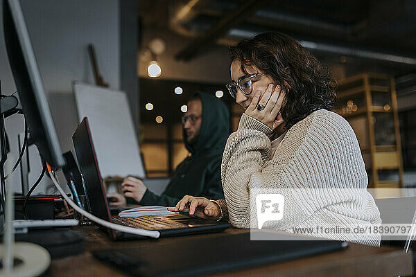 Junge Hackerinnen arbeiten am Laptop eines männlichen Kollegen am Schreibtisch eines Start-up-Unternehmens