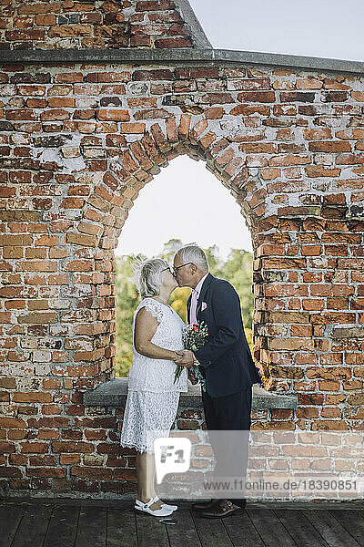 Romantic senior couple kissing on mouth by window during wedding