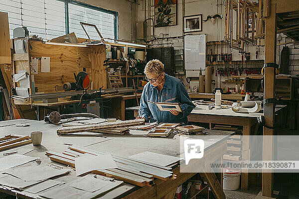 Älterer weiblicher Schreiner  der einen Rahmen hält  während er in der Werkstatt arbeitet