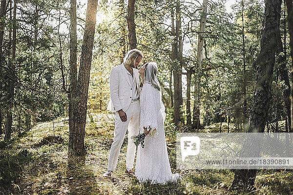 Die Braut schaut den Bräutigam an  während sie am Hochzeitstag inmitten von Bäumen im Wald steht