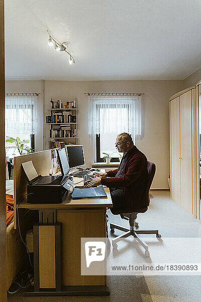 Seitenansicht eines älteren Mannes  der einen Computer am Schreibtisch im Heimbüro benutzt