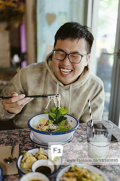 Glücklicher junger Mann  der im Restaurant mit Stäbchen isst