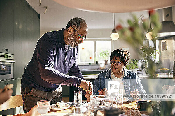 Senior man serving food to woman sitting at dining table in home
