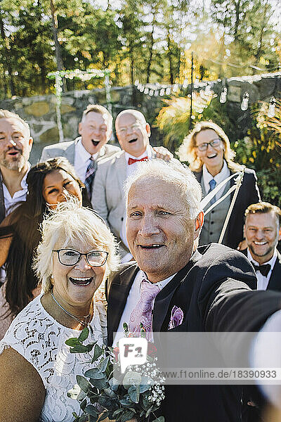 Fröhliches frisch verheiratetes älteres Paar  das ein Selfie mit Familie und Freunden bei der Hochzeit macht