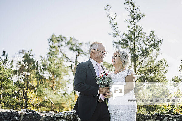 Lächelndes älteres Paar  das sich bei einer Hochzeit mit Blumenstrauß anschaut