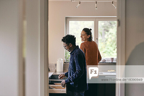 Glückliches gemischtrassiges Paar  das sich gegenseitig in der Küche zu Hause hilft